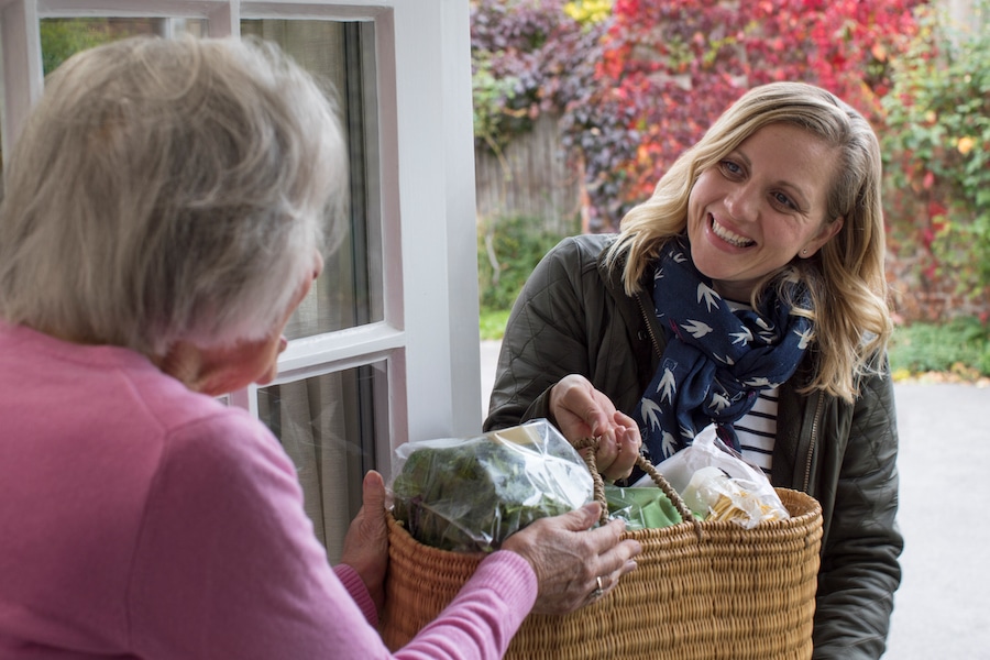 Female neighbor helping senior woman by delivering groceries to her apartment during the holidays