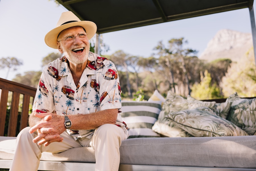 Vacationing after retirement. Happy elderly man laughing cheerfully while relaxing on a couch at a luxury spa resort. Carefree senior man enjoying himself while on a summer getaway.